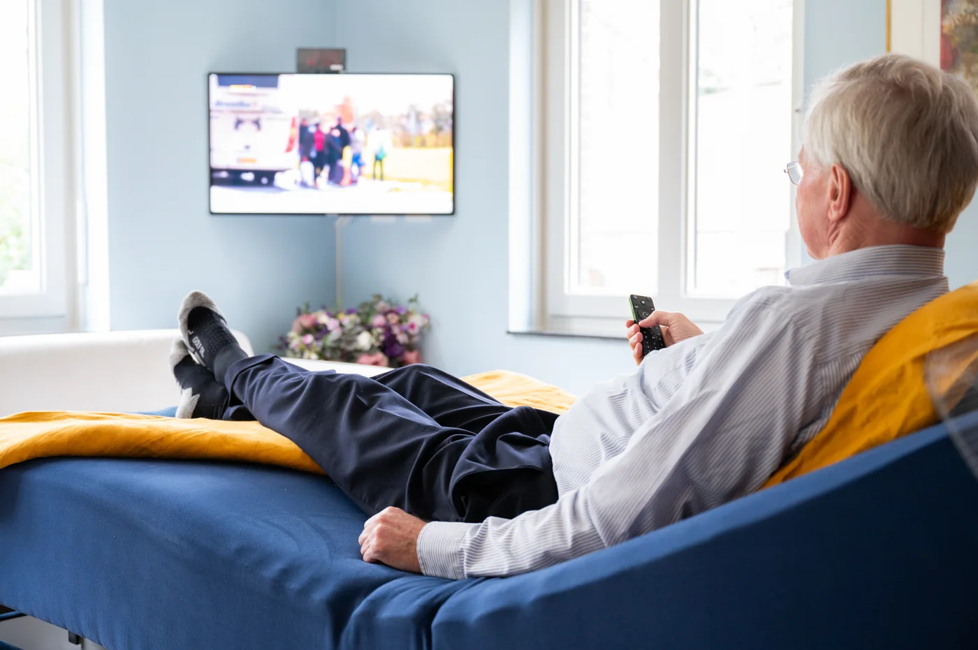 Luc ligt ontspannen op zijn bed met FPS en kijkt televisie